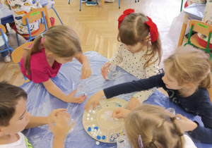 Dzieci wykonują serca - wrzucają pompony, brokat, błękitne i białe cekiny