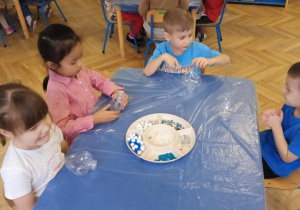 Dzieci wykonują serca - wrzucają pompony, brokat, błękitne i białe cekiny