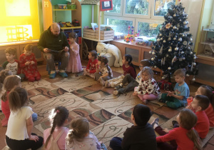 Dzieci siedzą w kole, słuchając książki czytanej przez tatę Marysi