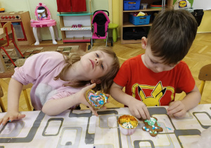dzieci siedzą przy stole i ozdabiają pierniki