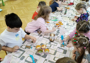 dzieci siedzą przy stole i ozdabiają pierniki