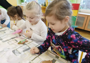 dzieci siedzą przy stole i ozdabiają pierniki