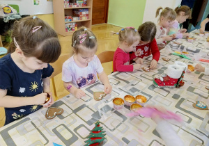 dzieci siedzą przy stole i ozdabiają pierniki