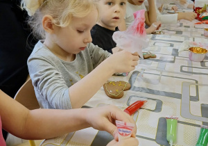 dzieci siedzą przy stole i ozdabiają pierniki