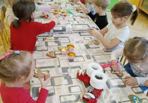 dzieci siedzą przy stole i ozdabiają pierniki