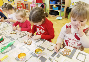dzieci siedzą przy stole i ozdabiają pierniki