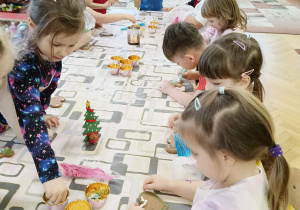 dzieci siedzą przy stole i ozdabiają pierniki