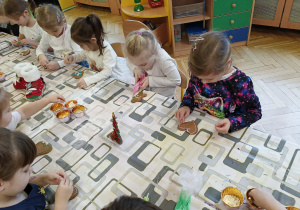 dzieci siedzą przy stole i ozdabiają pierniki