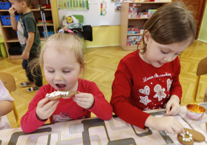dzieci siedzą przy stole jedzą i ozdabiają pierniki