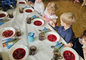dzieci wspólnie siedzą przy świątecznym stole, dzielą się opłatkiem