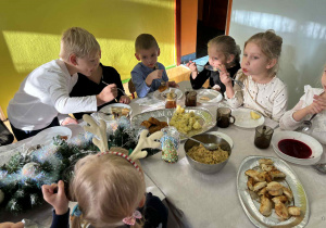 dzieci wspólnie siedzą przy świątecznym stole, spożywają potrawy