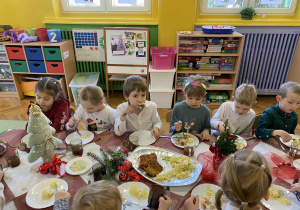 dzieci wspólnie siedzą przy świątecznym stole, spożywają potrawy