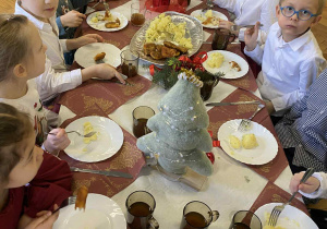 dzieci wspólnie siedzą przy świątecznym stole, spożywają potrawy