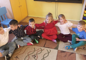 Dzieci siedzą na dywanie i wspólnie kolędują
