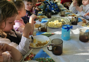 dzieci wspólnie siedzą przy świątecznym stole, spożywają potrawy