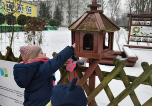 Dzieci wsypują ziarno dla ptaków do karmnika.