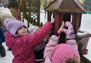 Dzieci wsypują ziarno dla ptaków do karmnika.