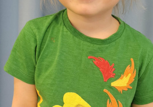 Dziewczynka prezentuje koszulkę z nadrukiem smoka.