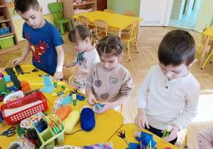 dzieci siedzą przy stolikach, wykonują kukiełki