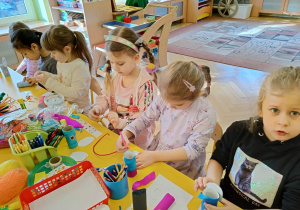 dzieci siedzą przy stolikach, wykonują kukiełki
