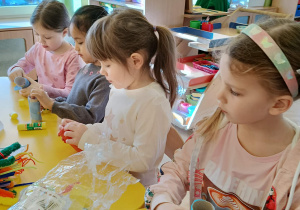 dzieci siedzą przy stolikach, wykonują kukiełki