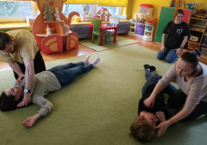 Rodzice ćwiczą na sobie na wzajem ułożenie w pozycji bocznej bezpiecznej.