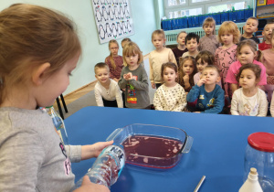 Dziewczynka wlewa zabarwiona wodę do naczynia.