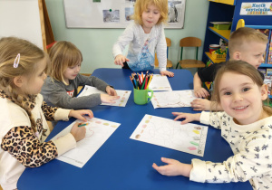 Dzieci siedzą przy stolikach, wykonują zadanie przy stolikach.