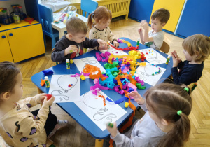 Dzieci siedzą przy stolikach, przy pomocy bibuły i kleju wyklejają baloniki.