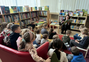 Dzieci siedzą na dywanie i słuchają pani czytającej książkę