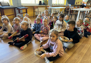 Dzieci siedzą na podłodze słuchając nauczyciela