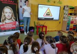 dzieci siedzą na dywanie, zapoznają się ze znakami drogowymi znajdującymi się przy przejazdach kolejowych