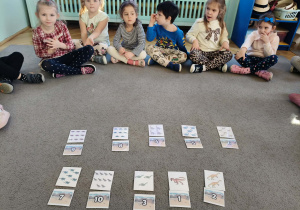 Dzieci siedzą w kole, uczestniczą w zabawie matematycznej: "Ile dinozaurów?".