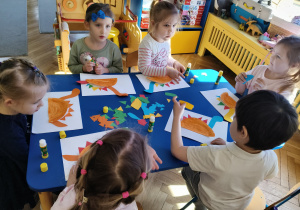 Dzieci siedzą przy stolikach i wykonują pracę plastyczną "Bajkowy dinozaur"