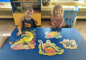 Dzieci prezentują ułożone przez siebie puzzle z dinozaurami.