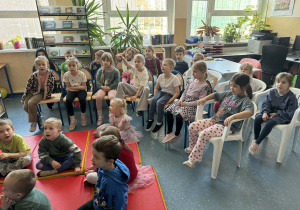 Dzieci siedzą na krzesełkach słuchając pani czytającej bajkę