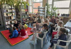 Dzieci siedzą na krzesełkach słuchając pani czytającej bajkę