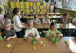 dzieci siedzą przy stolikach i wykonują pracę plastyczną- kwiatki