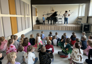 dzieci słuchają koncertu granego na fortepianie przez Tomka,