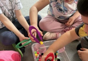 Dzieci w małych grupach nakładają szczypcami kulki w kolorach odpowiadających kolorze podstawy filiżanki.