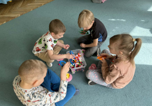 Dzieci w małych grupach nakładają szczypcami kulki w kolorach odpowiadających kolorze podstawy filiżanki.