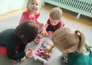 Dzieci w małych grupach nakładają szczypcami kulki w kolorach odpowiadających kolorze podstawy filiżanki.