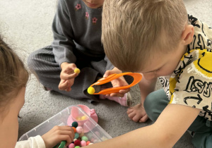 Dzieci w małych grupach nakładają szczypcami kulki w kolorach odpowiadających kolorze podstawy filiżanki.