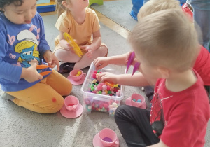 Dzieci w małych grupach nakładają szczypcami kulki w kolorach odpowiadających kolorze podstawy filiżanki.