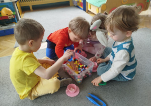 Dzieci w małych grupach nakładają szczypcami kulki w kolorach odpowiadających kolorze podstawy filiżanki.