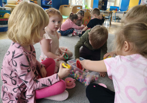 Dzieci w małych grupach nakładają szczypcami kulki w kolorach odpowiadających kolorze podstawy filiżanki.