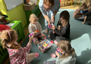 Dzieci w małych grupach nakładają szczypcami kulki w kolorach odpowiadających kolorze podstawy filiżanki.