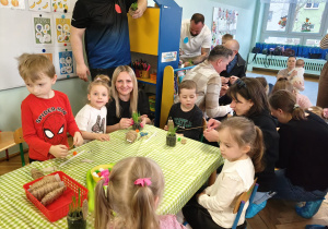 Rodzice wraz z dziećmi przy stołach wykonują wielkanocnego króliczka.