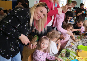 Rodzice wraz z dziećmi przy stołach wykonują wielkanocnego króliczka.