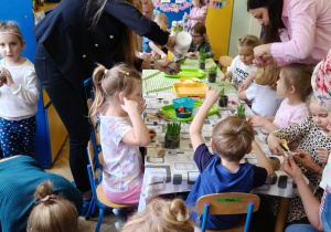 Rodzice wraz z dziećmi przy stołach wykonują wielkanocnego króliczka.